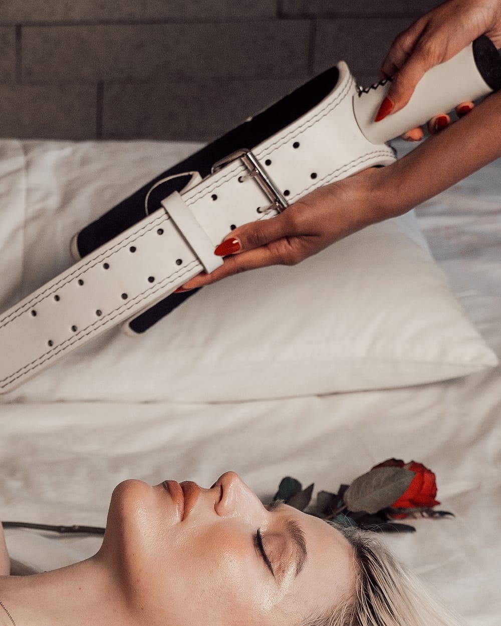 The white MunkeyBarz belt held above a bed scattered with roses
